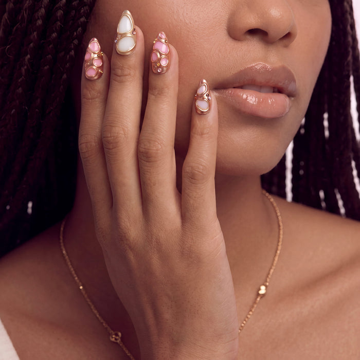 Model wearing Liquid Gold pink and white sculpted press-on nails with raised rose gold details near her face