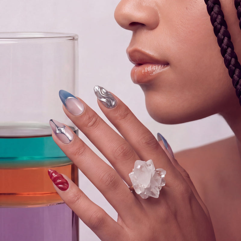 Hand model wearing Liquid Mercury press-on nails with silver chrome swirls, blue gray French tips, and glossy red accents