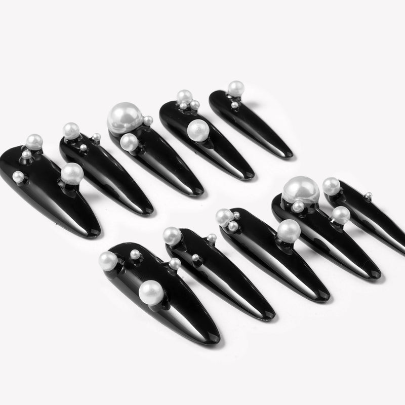 Diagonal flat lay of Louboutin Pearl Noir press-on nails with glossy black finish and pearl embellishments