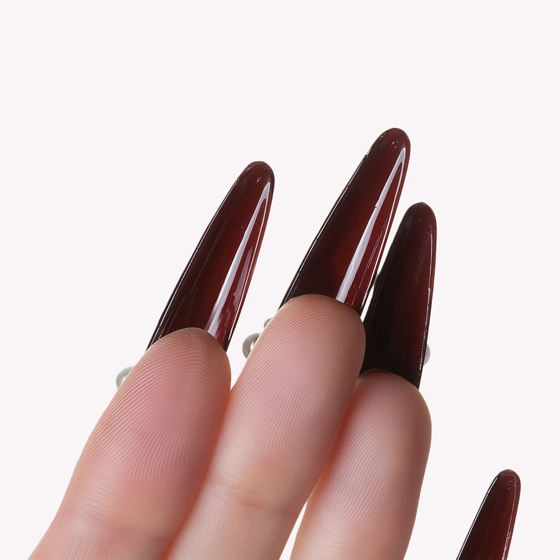 Hand model closeup wearing Louboutin Pearl Noir long burgundy press-on nails with pearl accents