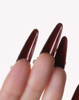 Hand model closeup wearing Louboutin Pearl Noir long burgundy press-on nails with pearl accents