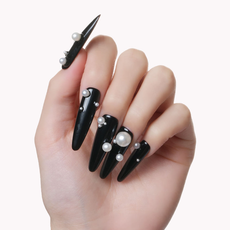Hand model wearing Louboutin Pearl Noir press-on nails with glossy black finish and pearl embellishments