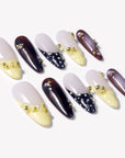 Flat lay of Lunar Velvet press-on nails with pale yellow tips, black dotted lattice designs, burgundy cat eye polish, pearls, and gold bead accents