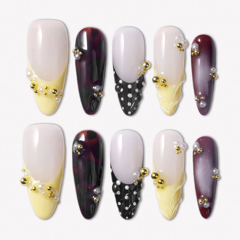 Lunar Velvet press-on nails with pale yellow tips, black dotted lattice designs, burgundy cat eye polish, gold beads, pearls, and glossy nude bases