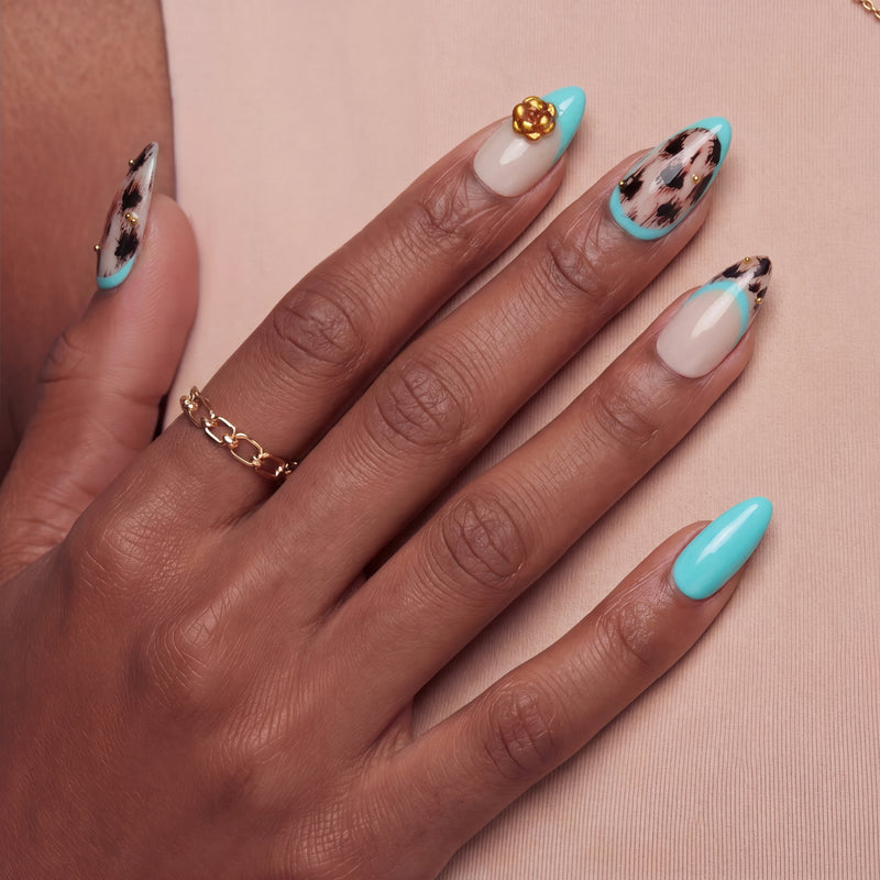 Close-up of a hand wearing turquoise and cream almond press-on nails with black abstract spots and a gold flower accent