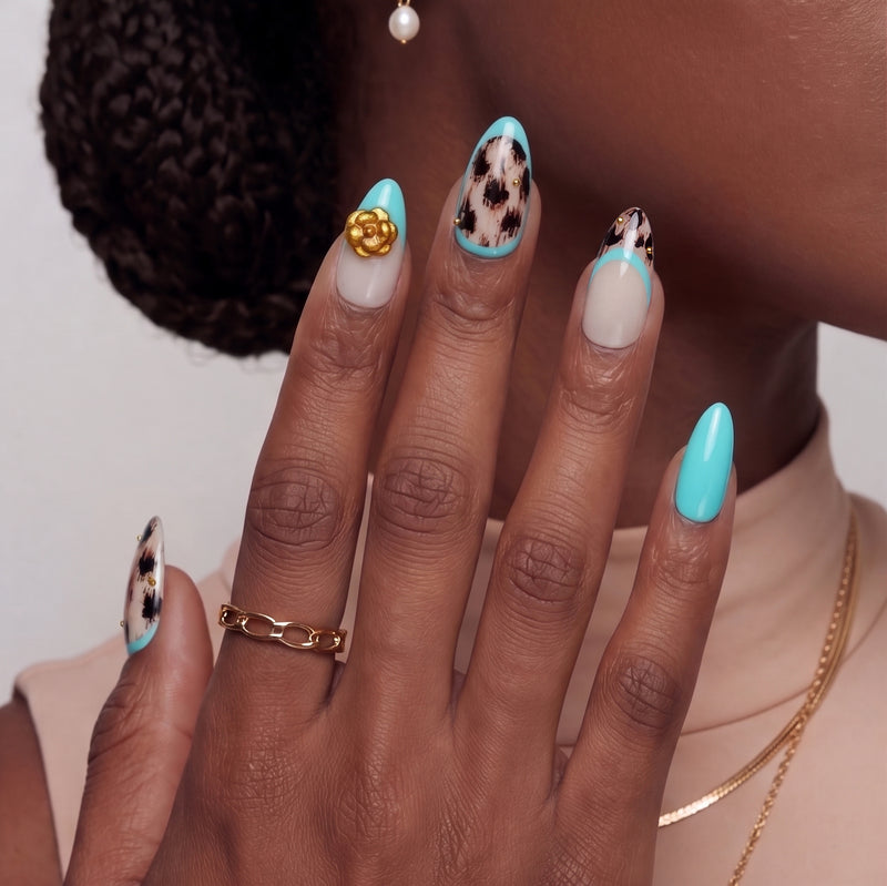 Hand model wearing turquoise and cream almond press-on nails with black abstract spots and a gold flower accent