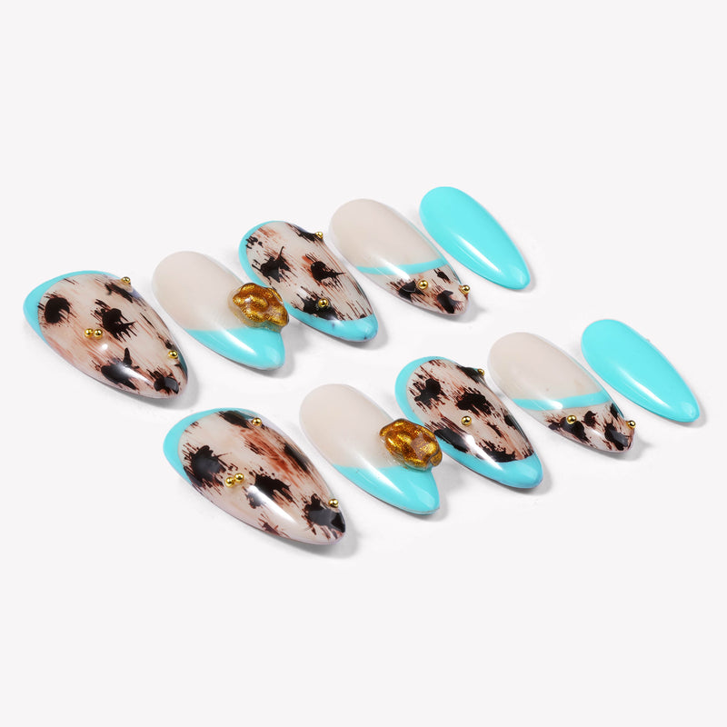 Two rows of turquoise and cream almond press-on nails with black abstract spots and gold flower accents arranged on a white background