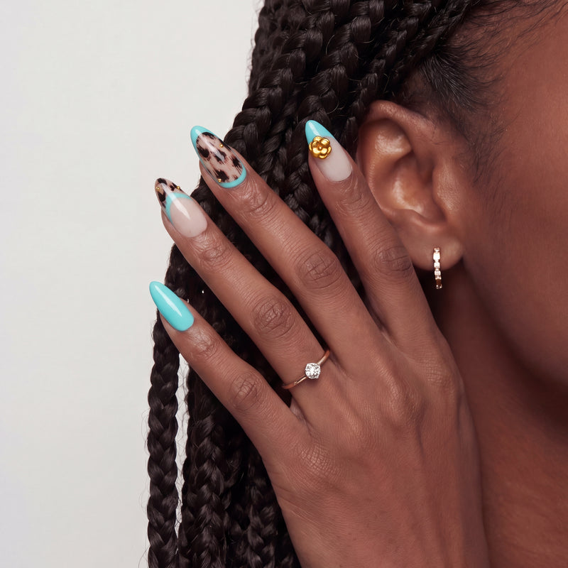 Side profile hand model wearing turquoise and cream almond press-on nails with black abstract spots and a gold flower accent
