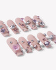 Angled flat lay of Luxurious Treasure press-on nails with nude pink square bases and large pink and clear rhinestone gems