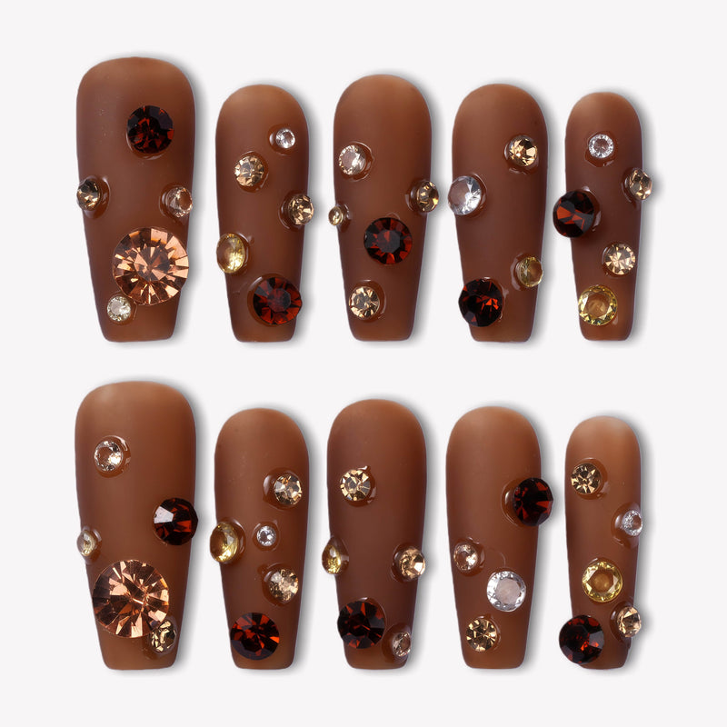 Flat lay of Luxurious Treasure press-on nails in a warm brown square style with gold, amber, and clear rhinestone gems