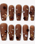 Flat lay of Luxurious Treasure press-on nails in a warm brown square style with gold, amber, and clear rhinestone gems