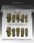 Packaging display of Luxurious Treasure olive green square press-on nails in a clear BeyondCanva case with large green, yellow, and clear rhinestone gems