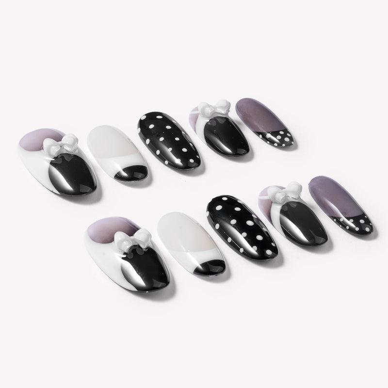 Flat lay of black and white press-on nails with polka dots and white bow accents arranged on a white background