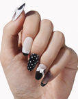 Hand model wearing black and white press-on nails with polka dots and white bow accents