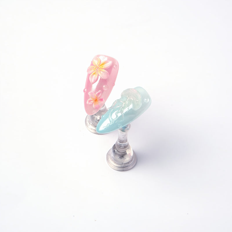 Detail display of Mermaid Mood pink flower and blue jellyfish press-on nails on clear stands