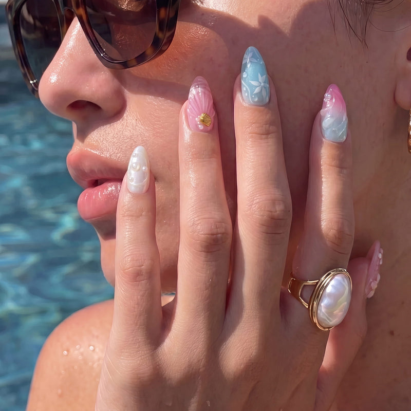 Poolside face close-up wearing Mermaid Mood pink and blue shell press-on nails with a pearl ring
