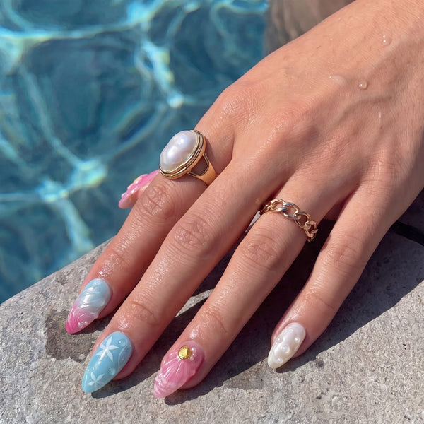 Poolside hand close-up wearing Mermaid Mood pink and blue shell press-on nails with pearl rings