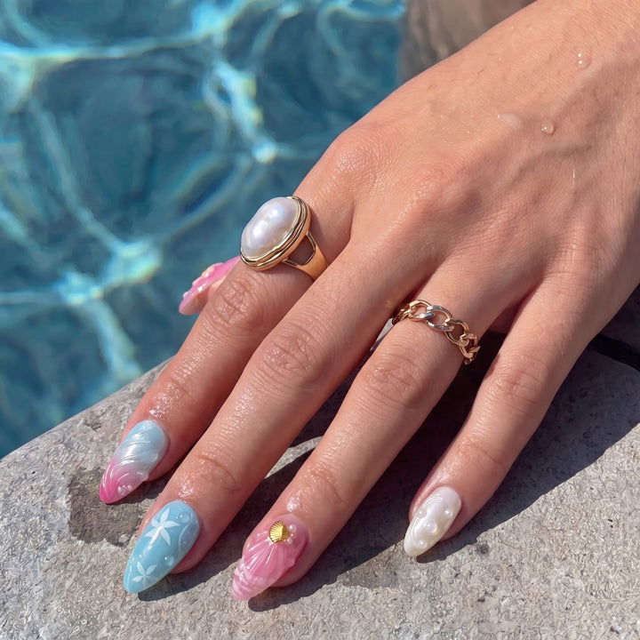 Poolside hand close-up wearing Mermaid Mood pink and blue shell press-on nails with pearl rings
