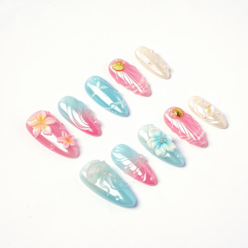 Angled flat lay of Mermaid Mood pink and blue shell nails with flowers, pearls and water drop accents