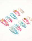 Angled flat lay of Mermaid Mood pink and blue shell nails with flowers, pearls and water drop accents