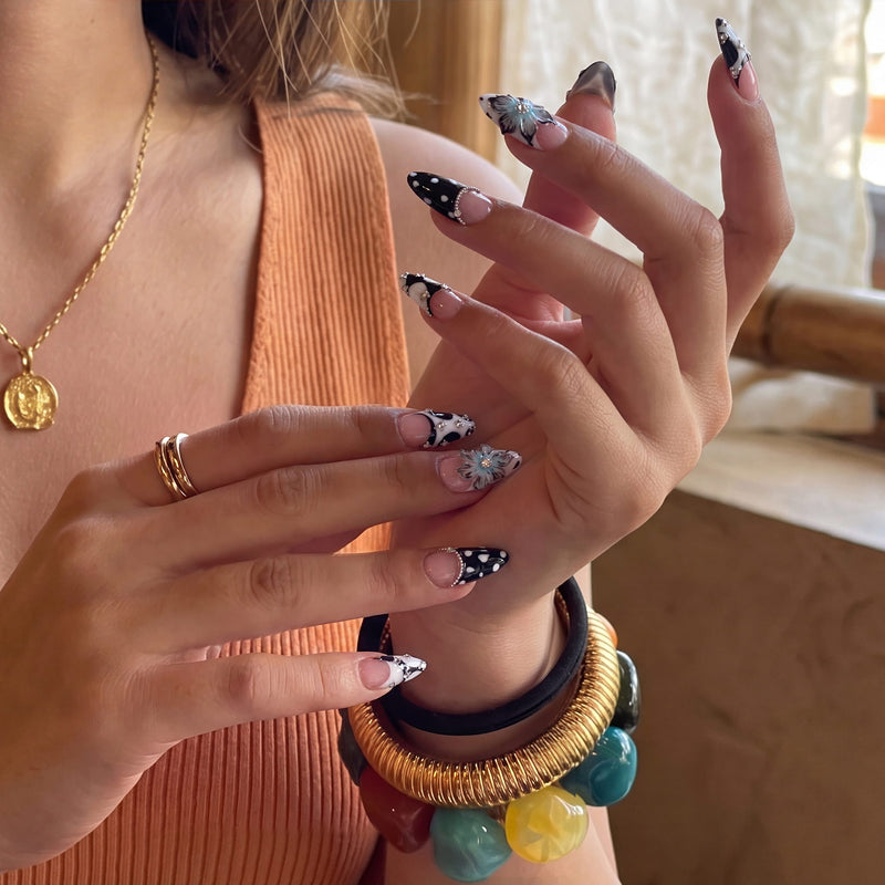 Hand model wearing Midnight Bloom pink, navy and white press-on nails with blue flower charms and rhinestones indoors