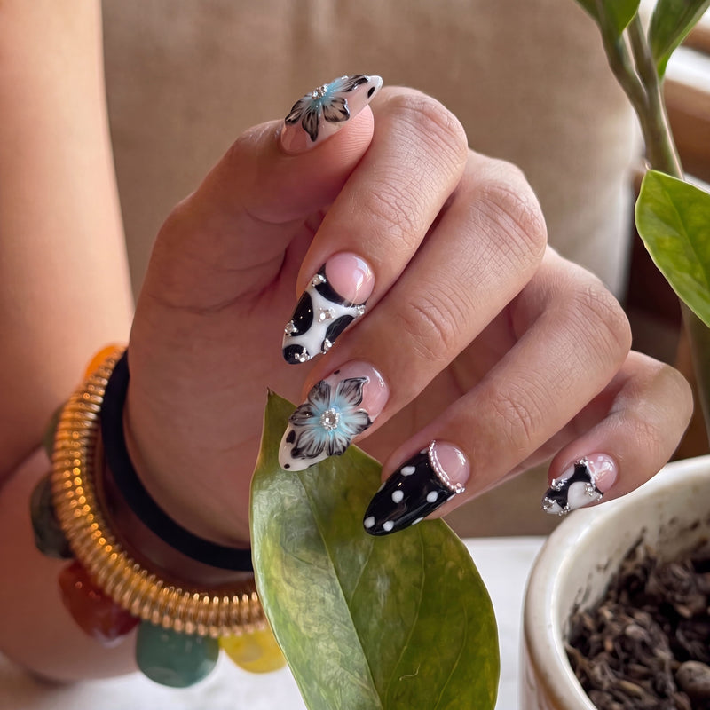 Close-up of Midnight Bloom pink and navy floral press-on nails with white polka dots and rhinestones beside a green plant