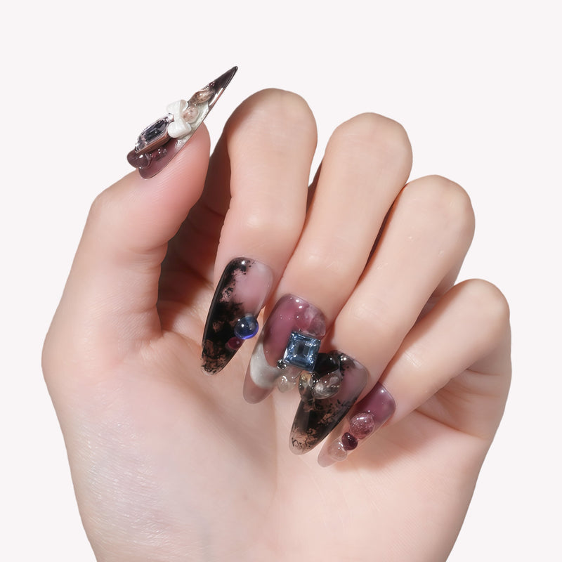 Hand model wearing Mineral Dreamscape press-on nails with lilac, black, and silver tones and gemstone accents