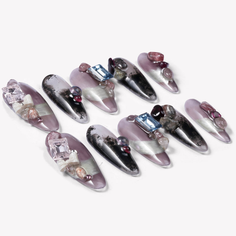 Flat lay of Mineral Dreamscape press-on nails arranged diagonally with lilac, black, silver, and gemstone accents