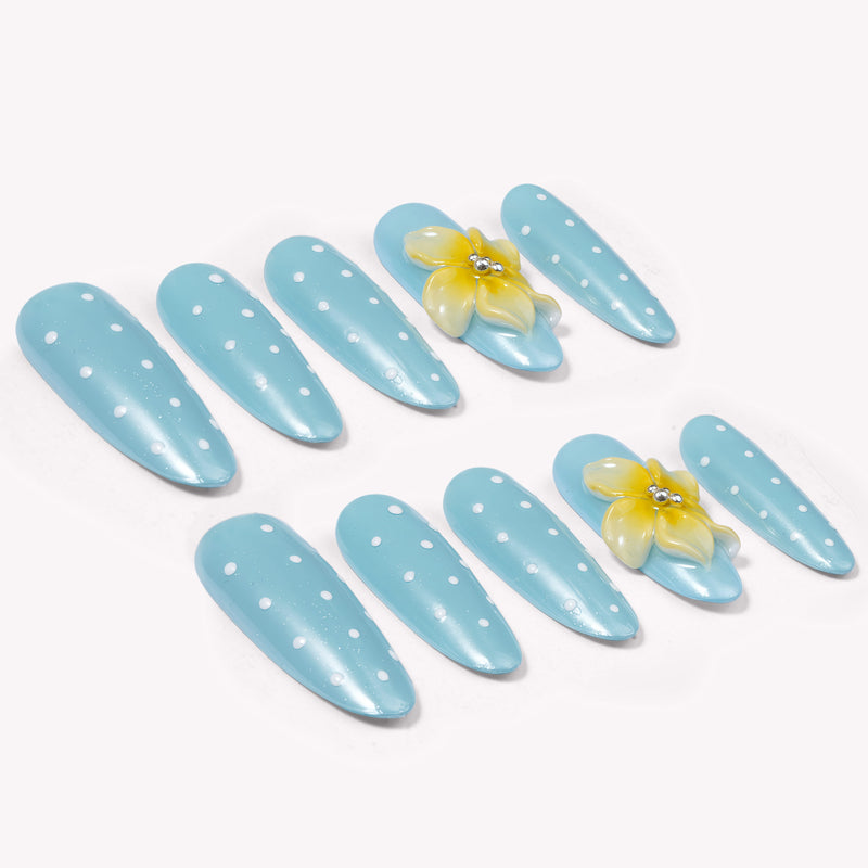 Diagonal flat lay of light blue polka dot press-on nails with yellow flower accents on a white background.