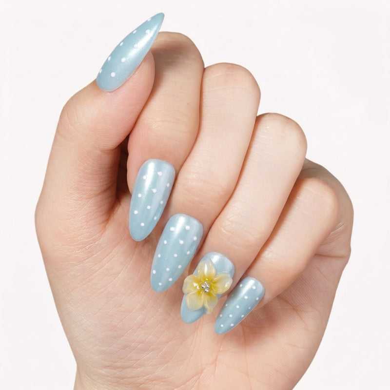 Hand model wearing light blue polka dot press-on nails with a yellow flower accent.