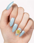 Hand model wearing light blue polka dot press-on nails with a yellow flower accent.