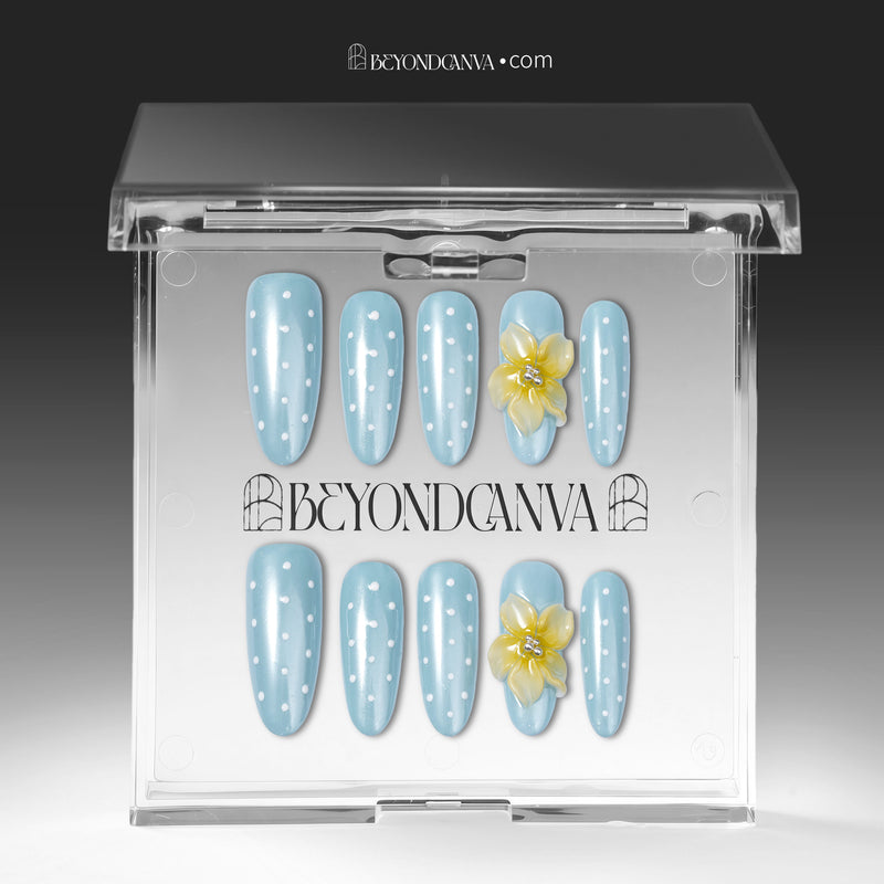 Press-on nails displayed in a clear BeyondCanva case with light blue polka dot nails and yellow flower accents.