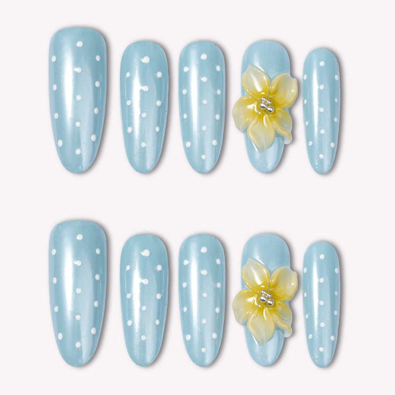 Flat lay of light blue polka dot press-on nails with a yellow flower accent on a white background.