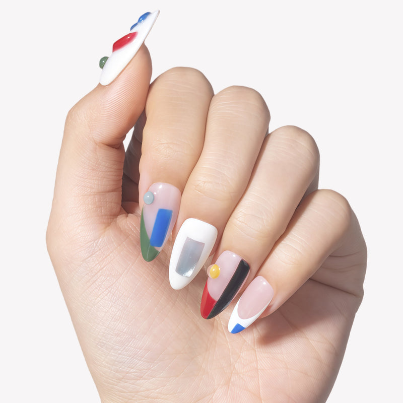 Hand model wearing Modernist Dream press-on nails with abstract red blue green black color blocks, raised round accents, and glossy nude white bases