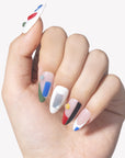 Hand model wearing Modernist Dream press-on nails with abstract red blue green black color blocks, raised round accents, and glossy nude white bases