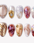 Molten Mirage press-on nails with amber red jelly swirls, champagne shimmer, gold shell accents, rhinestone trim, pearls, and iridescent gems
