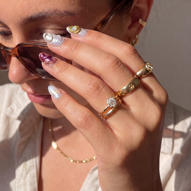 Hand model adjusting sunglasses while wearing Molten Mirage press-on nails with amber jelly swirls, gold framed gems, shimmer accents, and sculpted shell details