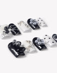 Angled flat lay of Monochrome Meow press-on nails with black and white cat designs, silver bow accents, pearl charms, polka dots, and happy heart lettering