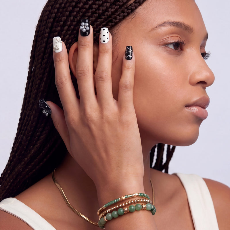 Side face close-up hand model wearing Monochrome Meow press-on nails with black and white cat designs, pearl charms, silver bow accents, and polka dots