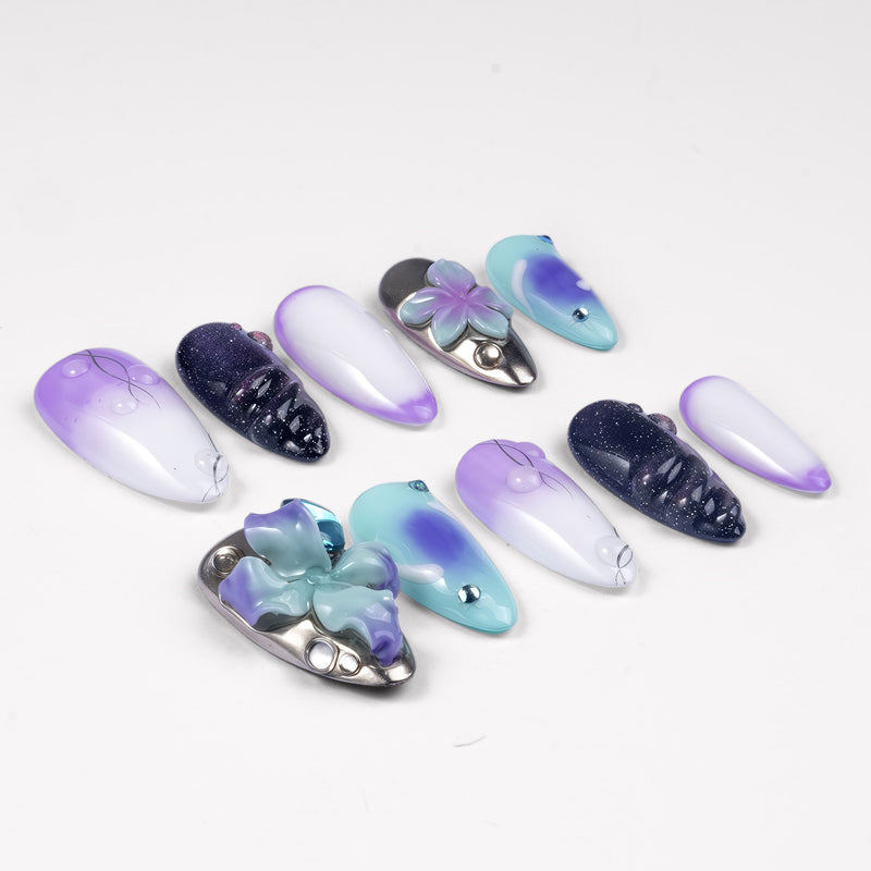 Angled flat lay of Moon Orchid purple, aqua, white and black press-on nails with raised orchids, blue gems and shimmer