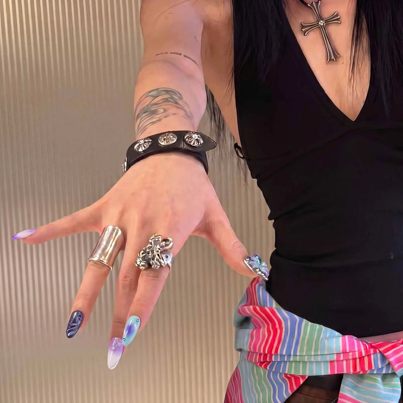 Hand model wearing Moon Orchid purple, aqua and black press-on nails with bold silver rings, bracelet and cross necklace