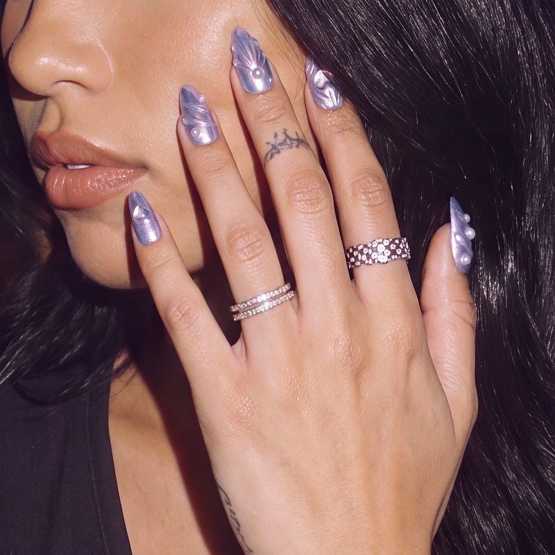Model wearing Moonwave blue purple iridescent press-on nails with pearl accents beside her face