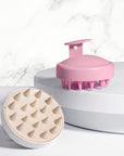 Pink and cream nail-friendly scalp massager brushes with flexible silicone tips displayed on white pedestals
