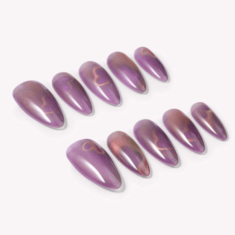 Angled flat lay of Nebula Kiss purple and pink cat-eye almond press-on nails with subtle glowing heart designs