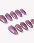 Angled flat lay of Nebula Kiss purple and pink cat-eye almond press-on nails with subtle glowing heart designs