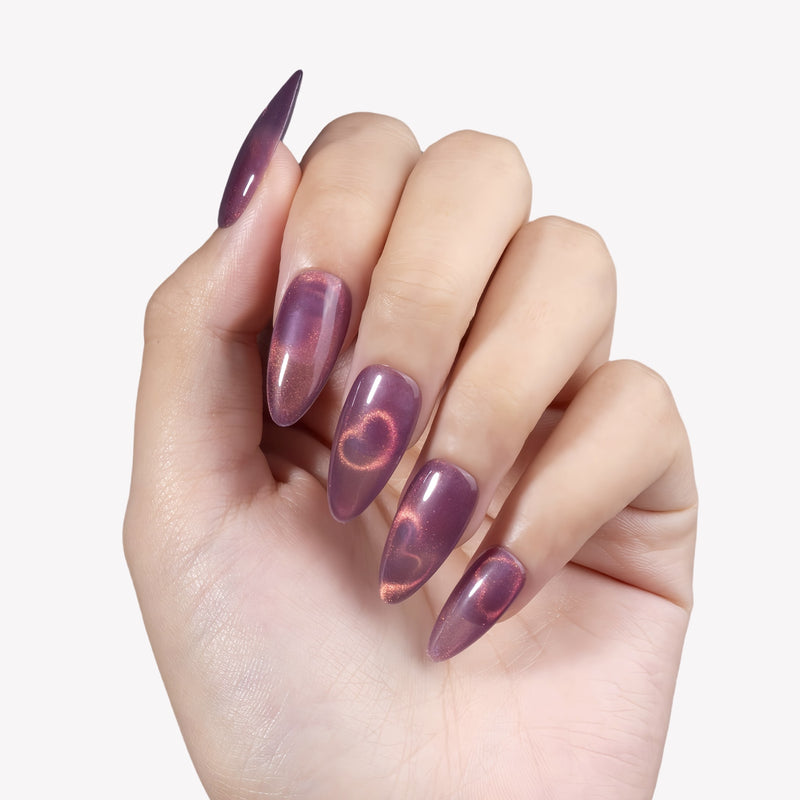 Close-up hand model wearing Nebula Kiss purple and pink cat-eye almond press-on nails with glowing heart accents