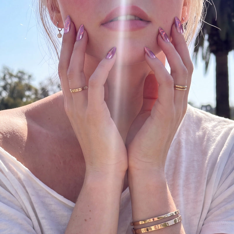 Nebula Kiss purple cat-eye almond press-on nails with pink heart accents shown on an outdoor model in sunlight