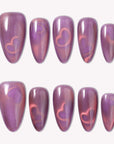 Nebula Kiss purple and pink cat-eye press-on nails with glowing heart accents arranged in a white flat lay