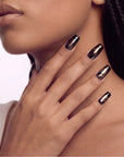 Portrait of a hand model wearing Nocturne Gild press-on nails in glossy black with metallic gold foil accents