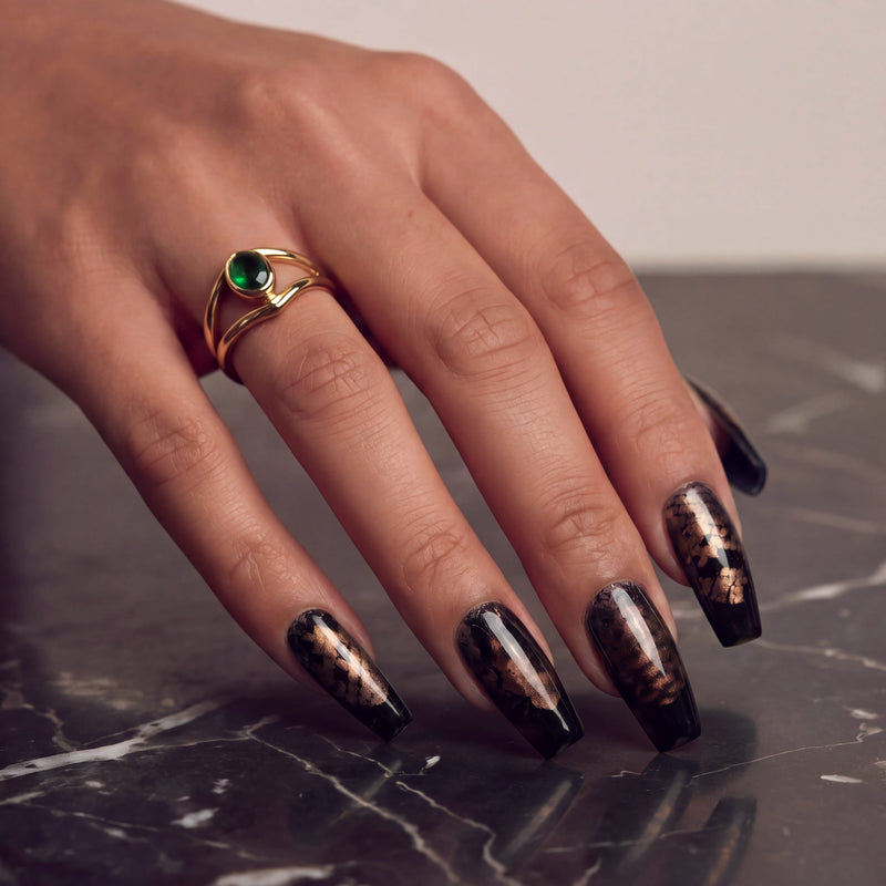 Hand model wearing Nocturne Gild press-on nails in glossy black with metallic gold foil accents